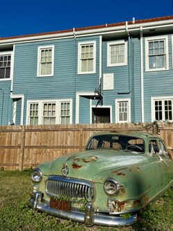 Beautiful greenish vintage Oldtimer Car in front of blue wooden House